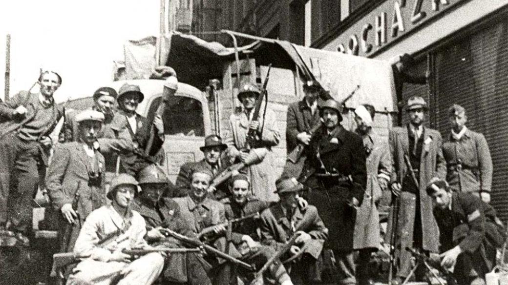 Bojovníci pražského povstání vyzbrojení puškami, pancéřovými pěstmi, sedící muž uprostřed italským samopalem Bereta a vpravo dole je lehký kulomet vz.26