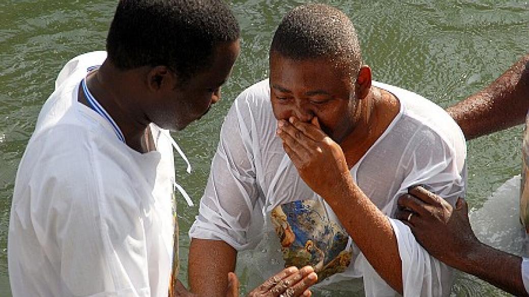 Poutníci procházejí křtem v řece Jordán
