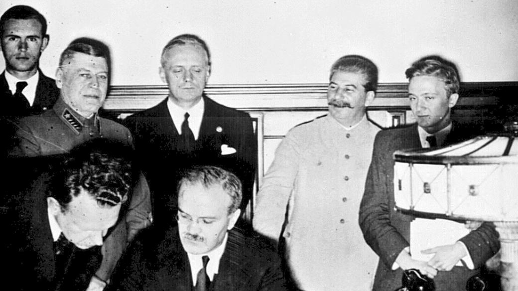 Molotov podepisuje německo-sovětskou smlouvu o neútočení. Za ním je vidět Ribbentrop (v černém) a Stalin (ve světlém, druhý zprava)