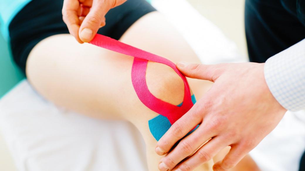 Fyzioterapeut aplikuje ženě na koleno kinesiotape