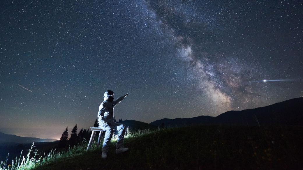 Osvětlený muž v bílém obleku a helmě, Mléčná dráha, hvězdná obloha, noc. Kosmické cestování, kosmonautika (ilustrační foto)