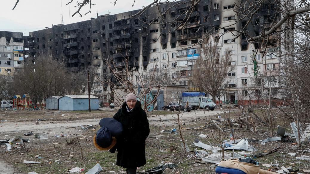 Žena prochází poničenou obytnou zónou v ukrajinském Mariupolu
