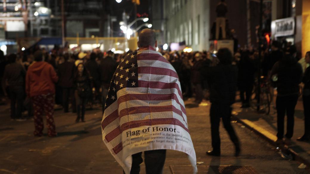 Muž s vlajkou USA míří k davu oslavujícímu smrt Usámy bin Ládina na Ground Zero v New Yorku (archivní foto, 2. května 2011)