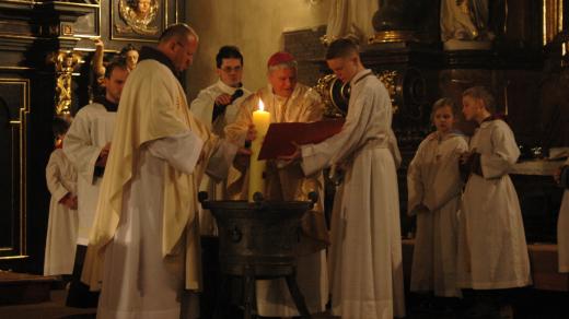 Biskup Václav Malý noří velikonoční svíci do křestní vody