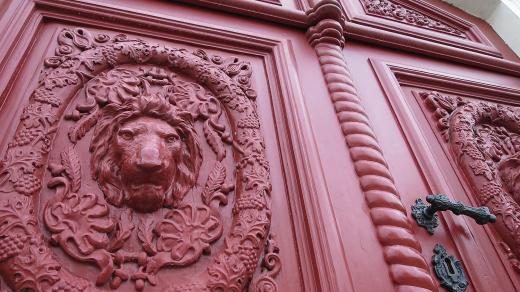 Vrata bývalého hostince čp. 184 na Palackého náměstí, litinové lví hlavy ve věnci z vinných listů a hroznů