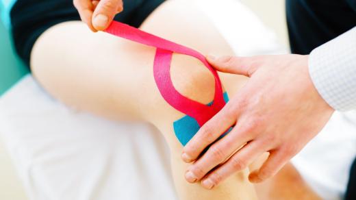 Fyzioterapeut aplikuje ženě na koleno kinesiotape
