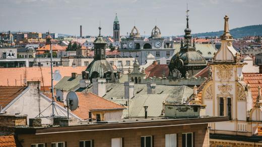 Plzeňské střechy s věží Mrakodrapu na Americké třídě uprostřed snímku. Střechu zdobí dvě nástavby s hodinami a dvě věže ve tvaru koruny, které vzdáleně připomínají střechy soudobých amerických mrakodrapů
