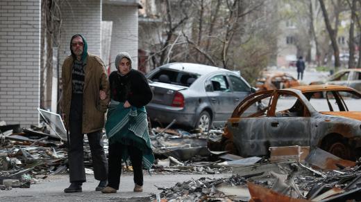 Obyvatelé Mariupolu procházejí kolem zničených aut