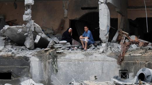 Palestinci sedí mezi troskami poškozené budovy po izraelských úderech ve městě Gaza
