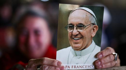 Člověk drží obraz papeže Františka v den modlitební bohoslužby na Svatopetrském náměstí