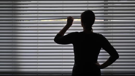 Žena vyhlíží z okna přes žaluzie