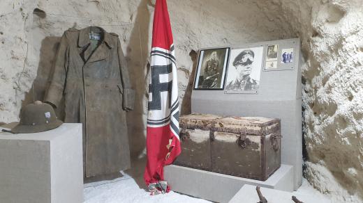 V celé jeskyni jsou prakticky jen tři vitríny. Hned v první je několik fotografií Erwina Rommela, je tu jeho osobní helma, kabát, dvě pistole