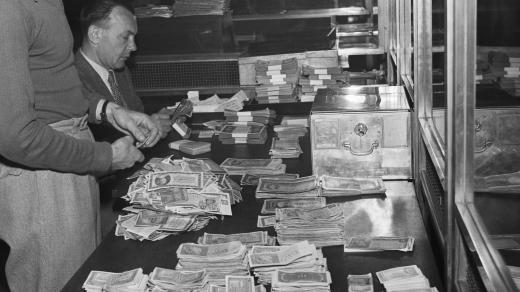 Měnová reforma /30. května 1953 schválilo NS zákon o peněžní reformě. Čs. občané přicházejí do výměnných středisek, aby si vyměnili staré peníze za novou měnu. Na sn. bankovní úředníci přepočítávají staré peníze/