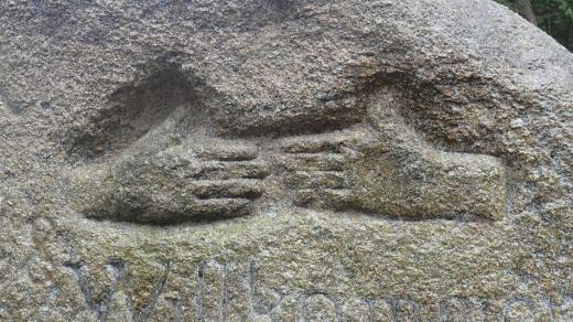 Do kamene jsou vytesané dvě ruce spojující se při usmíření