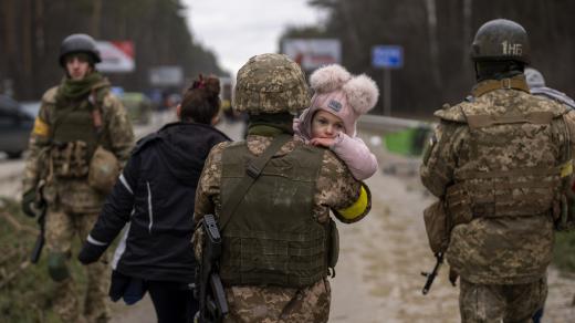 Ukrajinský voják nese dítě, aby pomohl prchající rodině překročit řeku Irpin na okraji Kyjeva