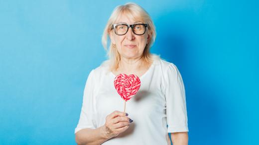 Starší žena s brýlemi drží v rukou lízátko ve tvaru srdce
