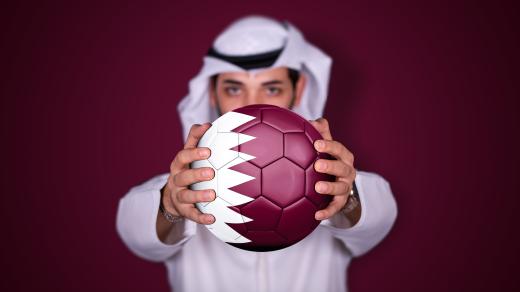 Arab držící fotbalový míč s katarskou vlajkou